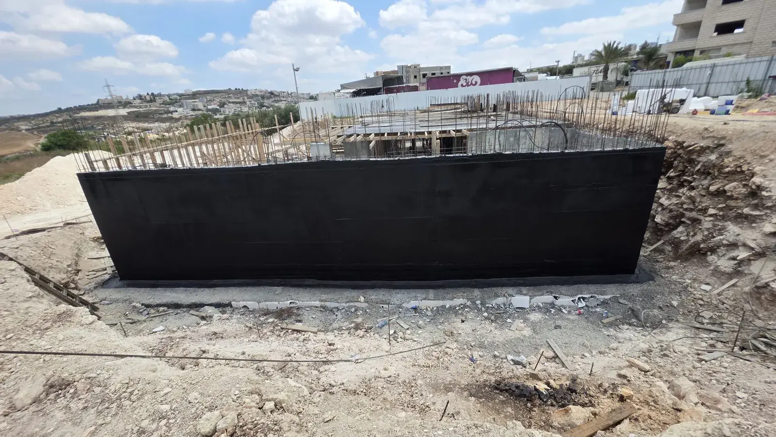 קיר מרתף ארוך מצופה בשכבת איטום שחורה, בתוך חפירה פתוחה באתר בנייה